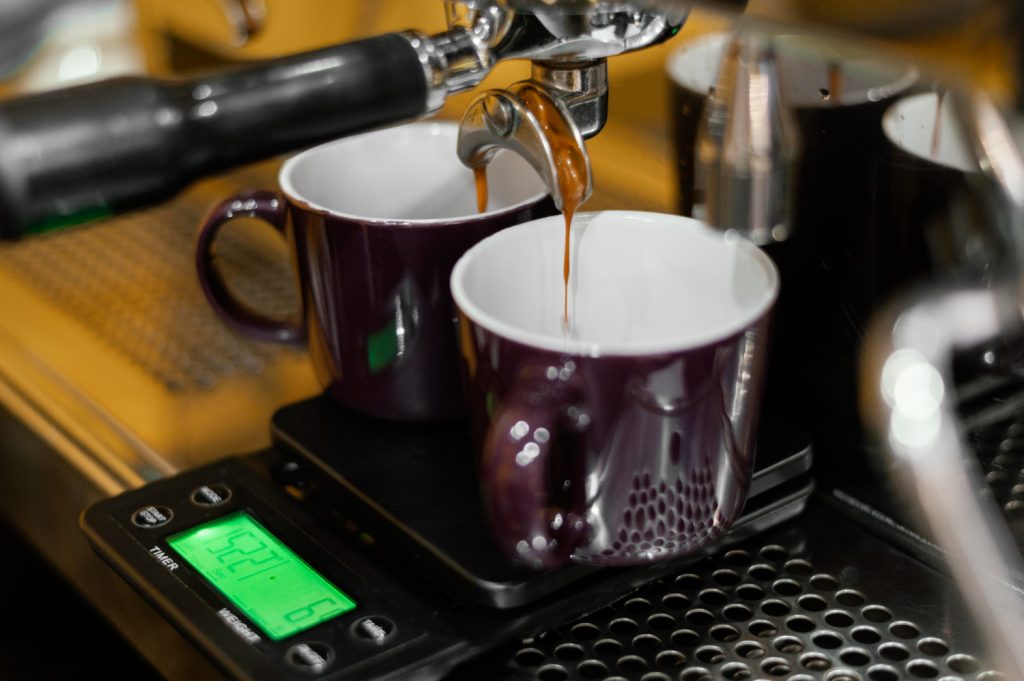 Rich espresso pouring from a machine into two purple mugs on a digital scale, capturing the coffee-making process and Indonesia’s Coffee Production.