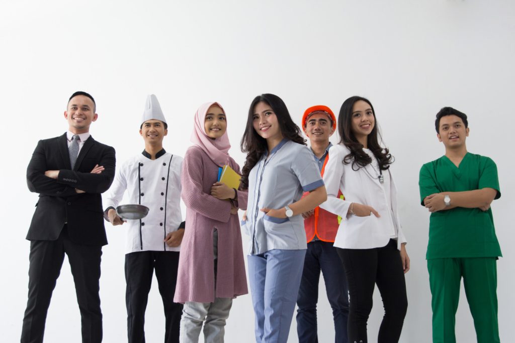 A diverse group of professionals Indonesian Migrant Workers in various uniforms, including a chef, nurse, and business attire, posing confidently against a white background.