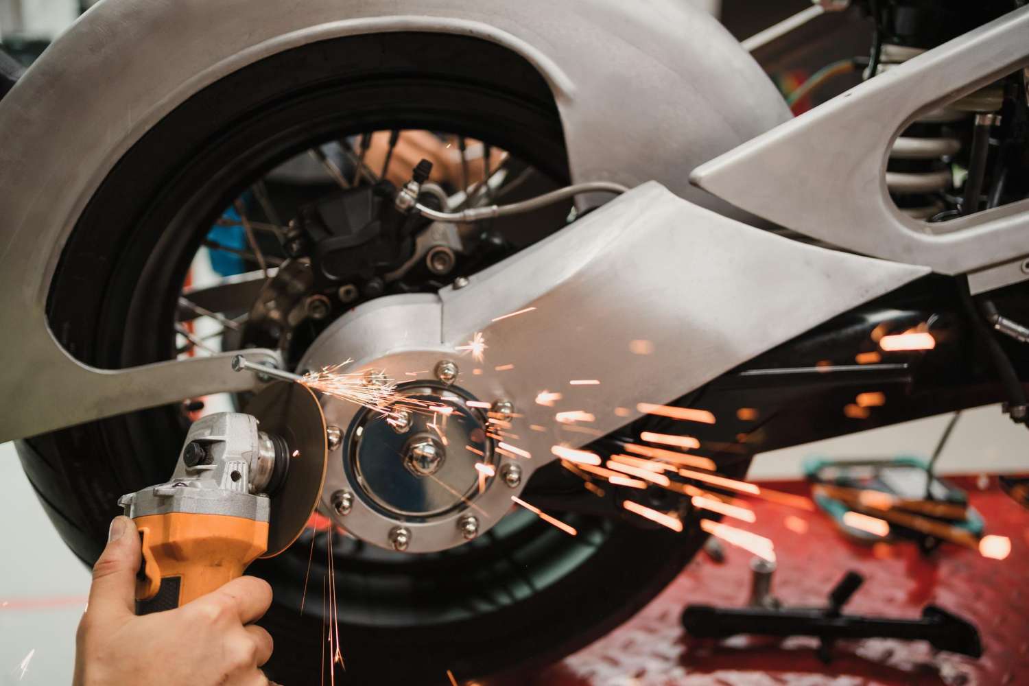 A mechanic uses a grinding tool on a motorcycle's metallic parts, creating sparks in a workshop setting.