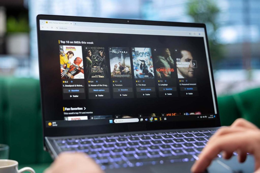 A laptop screen displays a list of the top 10 movies on IMDb for the week, featuring titles and ratings, with a coffee cup nearby.
