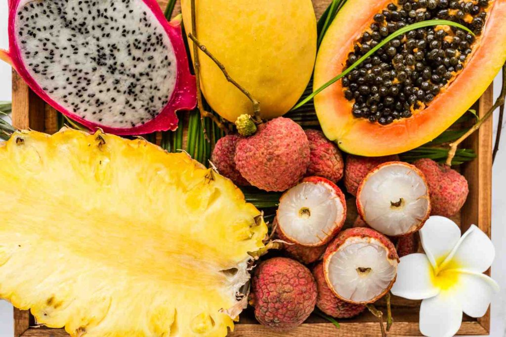 A vibrant assortment of tropical fruits including dragon fruit, mango, lychee, pineapple, and papaya, accented with a white flower.
