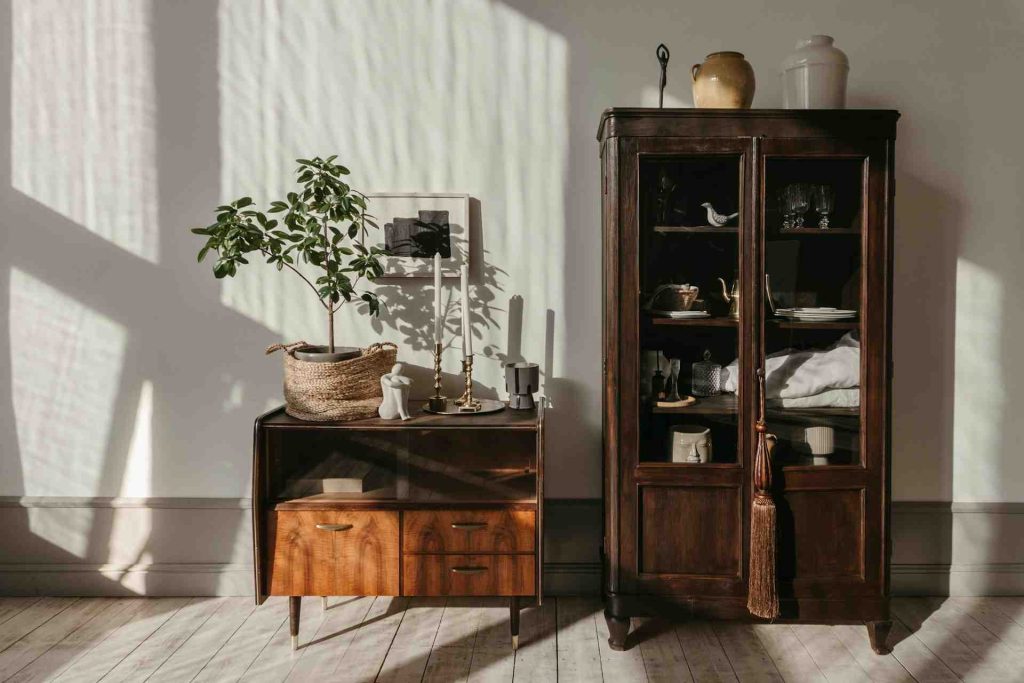 Cozy interior featuring a wooden cabinet, a modern side table with a plant, candles, and warm sunlight casting shadows.
