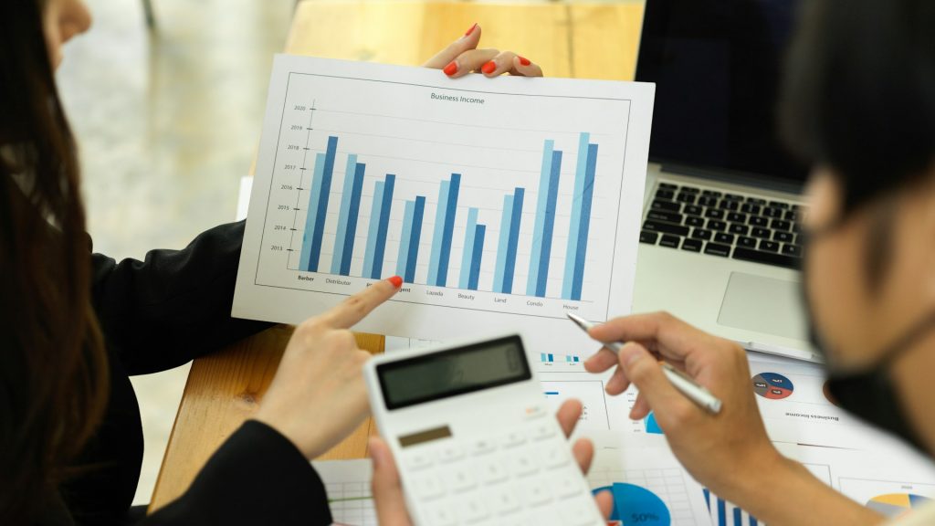 Central Insight Market Expansion: Two professionals analyzing a business income graph while using a calculator and pointing to data on printed reports.